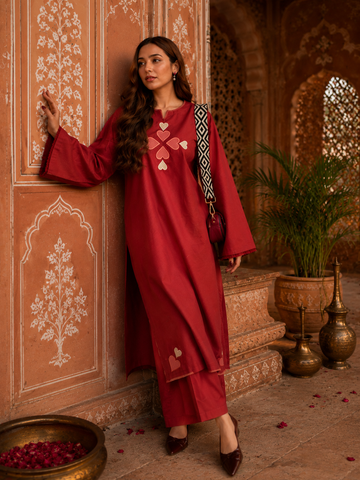 Woman wearing red cotton Pakistani style co-ord set with heart embroidery standing beside textured wall